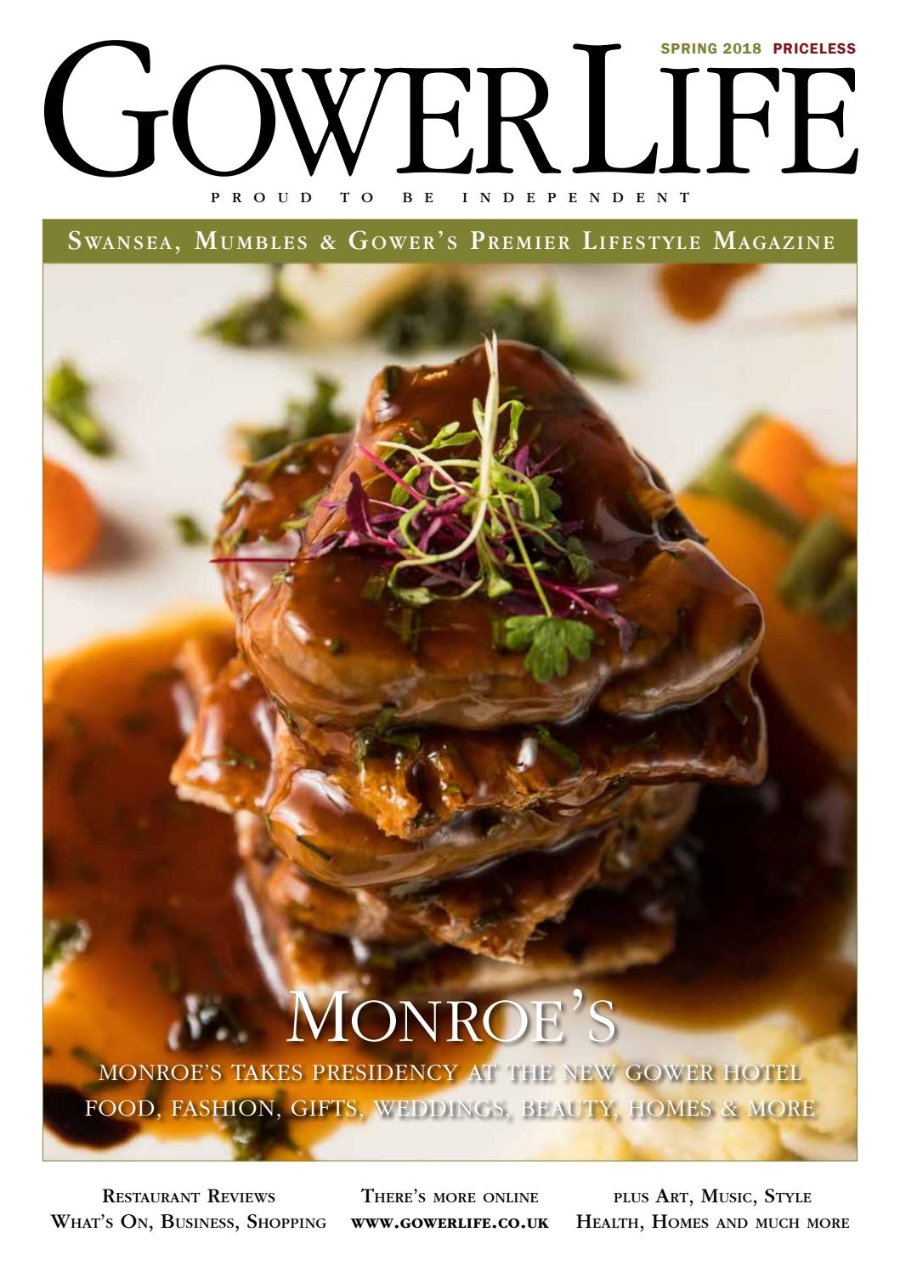 Gower Life Spring 2018 cover. A close-up of a tall stack of slow-cooked meat glazed in a glossy dark sauce, topped with micro herbs and fine shoots, on a white plate with vegetables blurred behind. Headline: Monroe's.